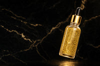 24K Gold Serum floating on black and gold marble